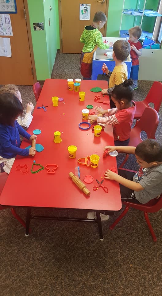 Children playing with modeling clay at a red table in a classroom