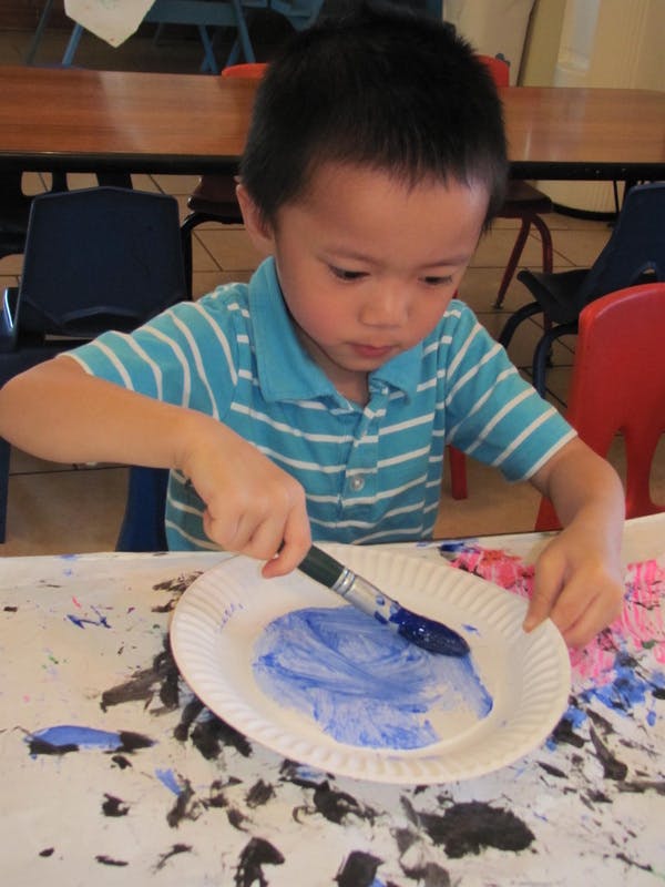 Child painting blue on a paper plate with a paintbrush