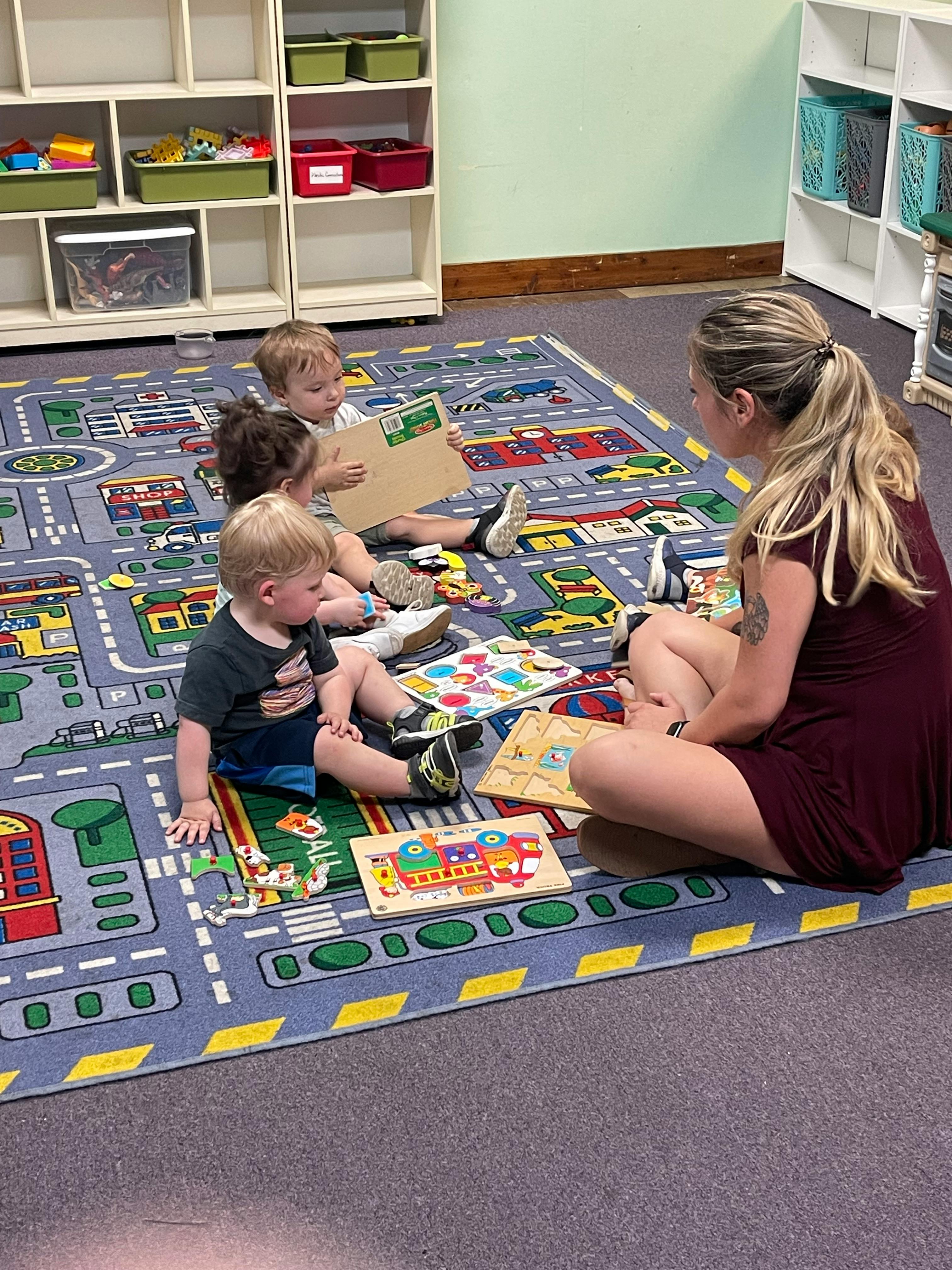 Adult and three children sitting on a rug with puzzles and books