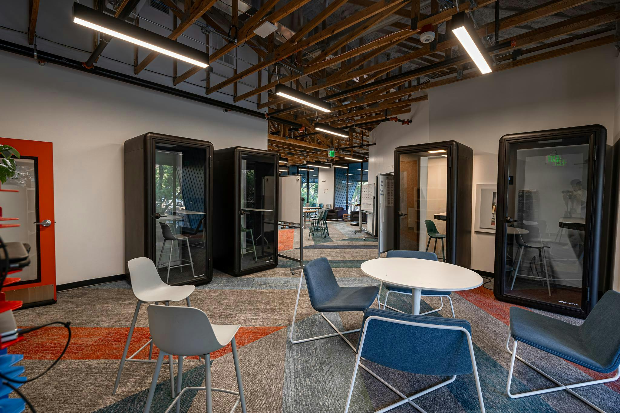 An office space with acoustic pods, a small round table with chairs, and patterned carpet
