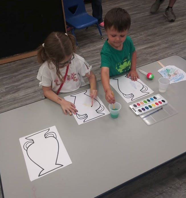 Two children painting vase outlines with watercolors at a table