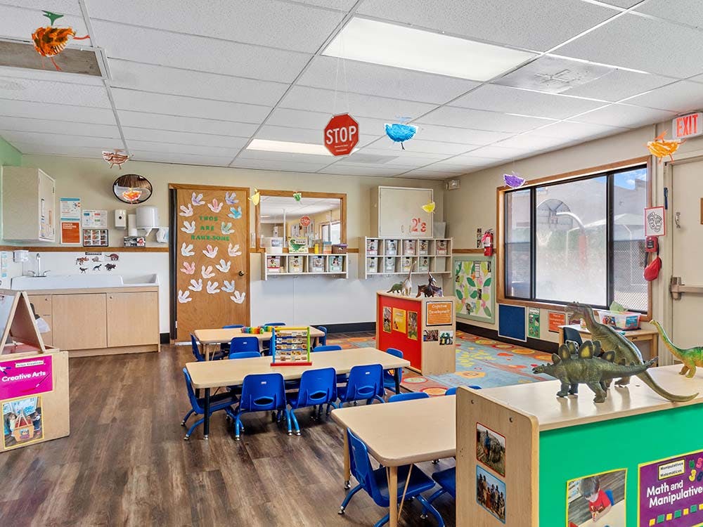 Classroom with tables, chairs, dinosaur toys, and artwork on the walls