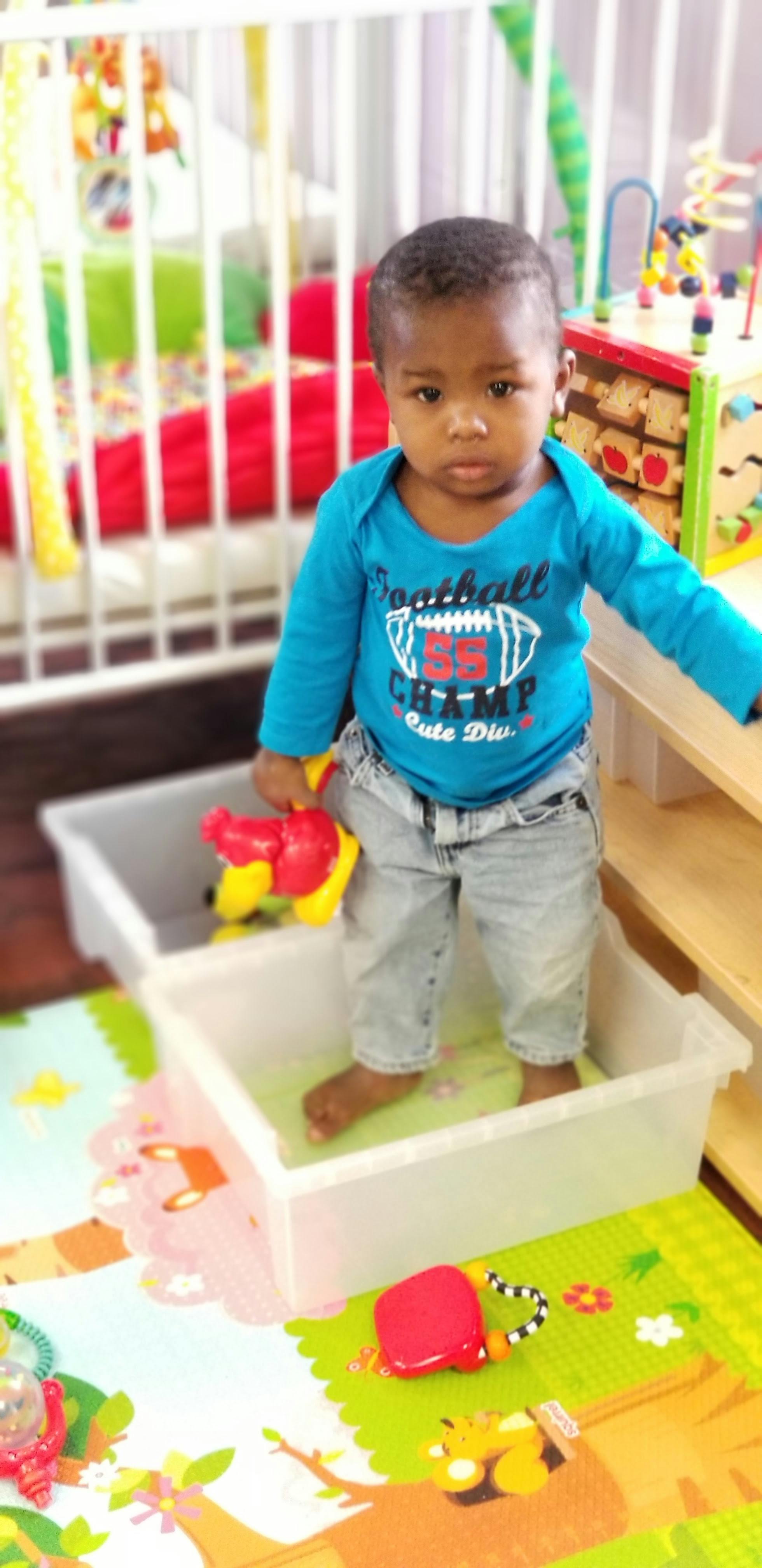 Child standing in a plastic bin holding a toy
