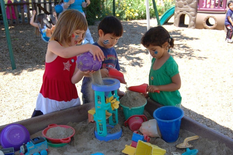 Three children playing in a sandbox with toys
