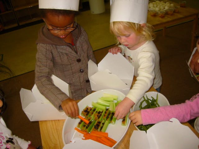 Two children in chef hats preparing vegetables