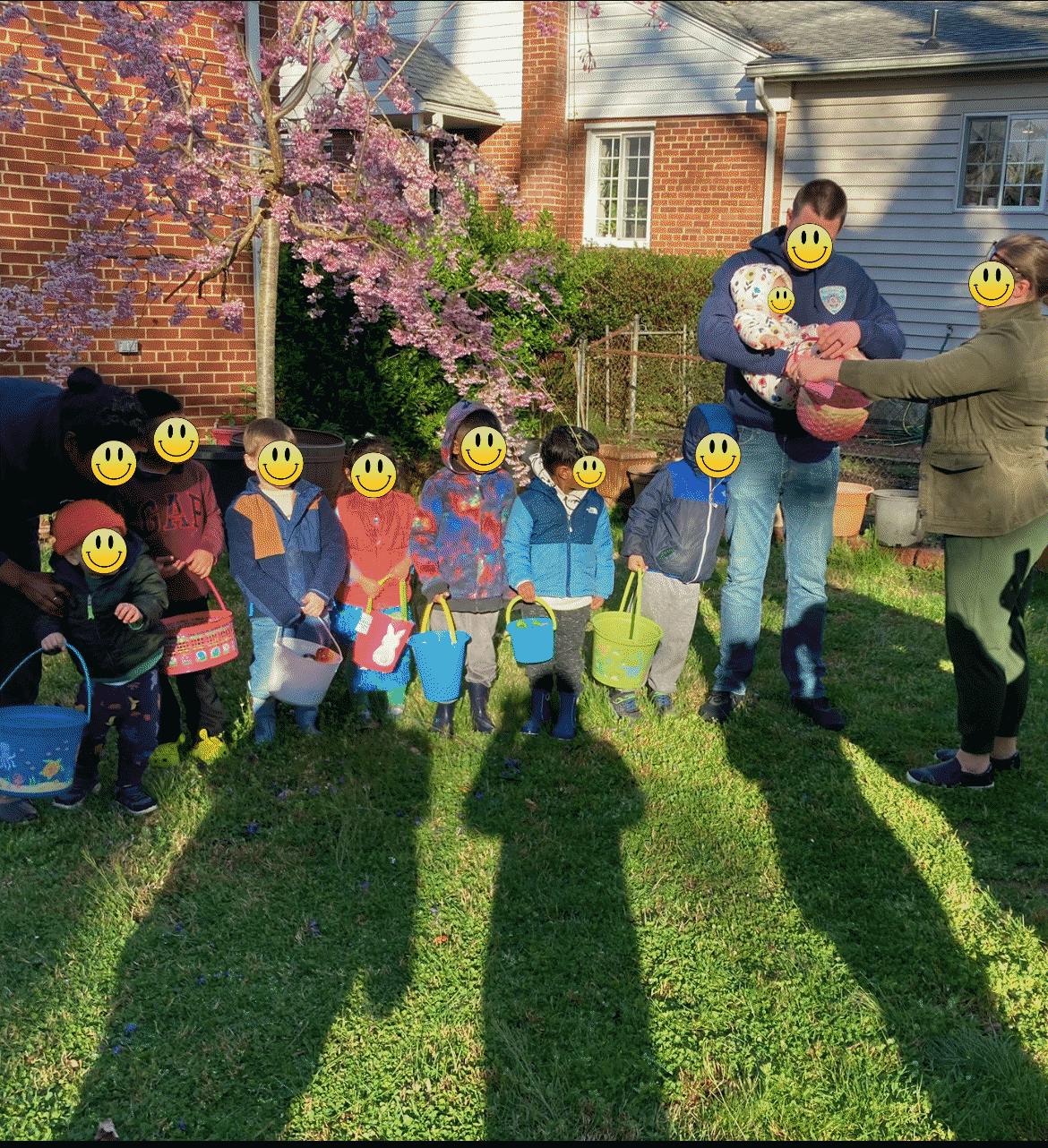 Group of children holding baskets with adults on a lawn near a flowering tree