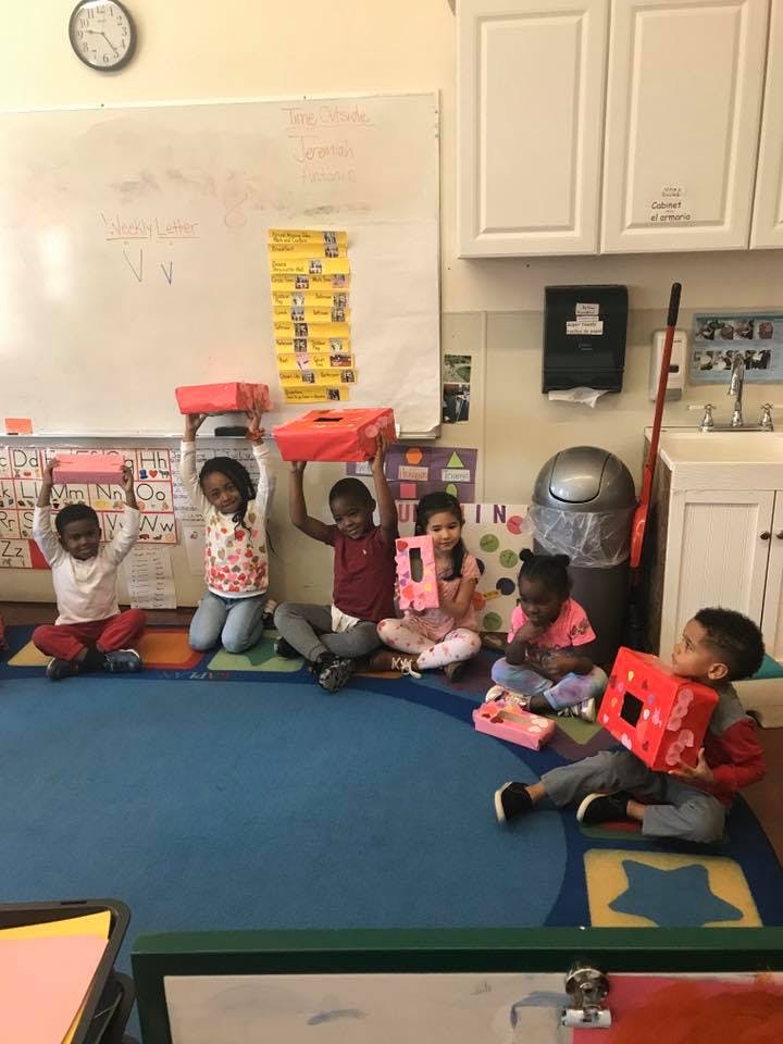 Children sitting on a rug holding up red boxes