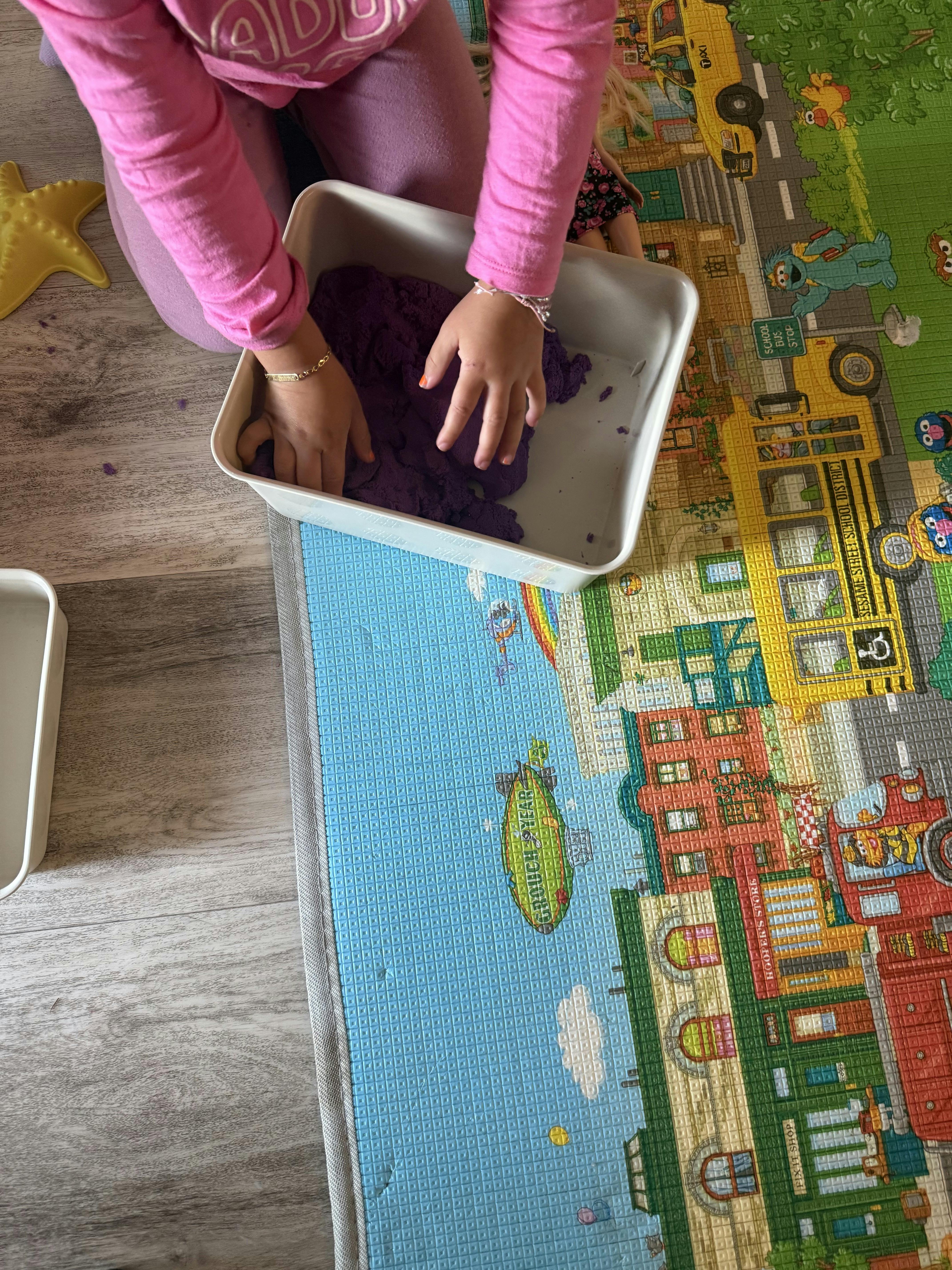 Child playing with purple kinetic sand in a plastic bin on a play mat