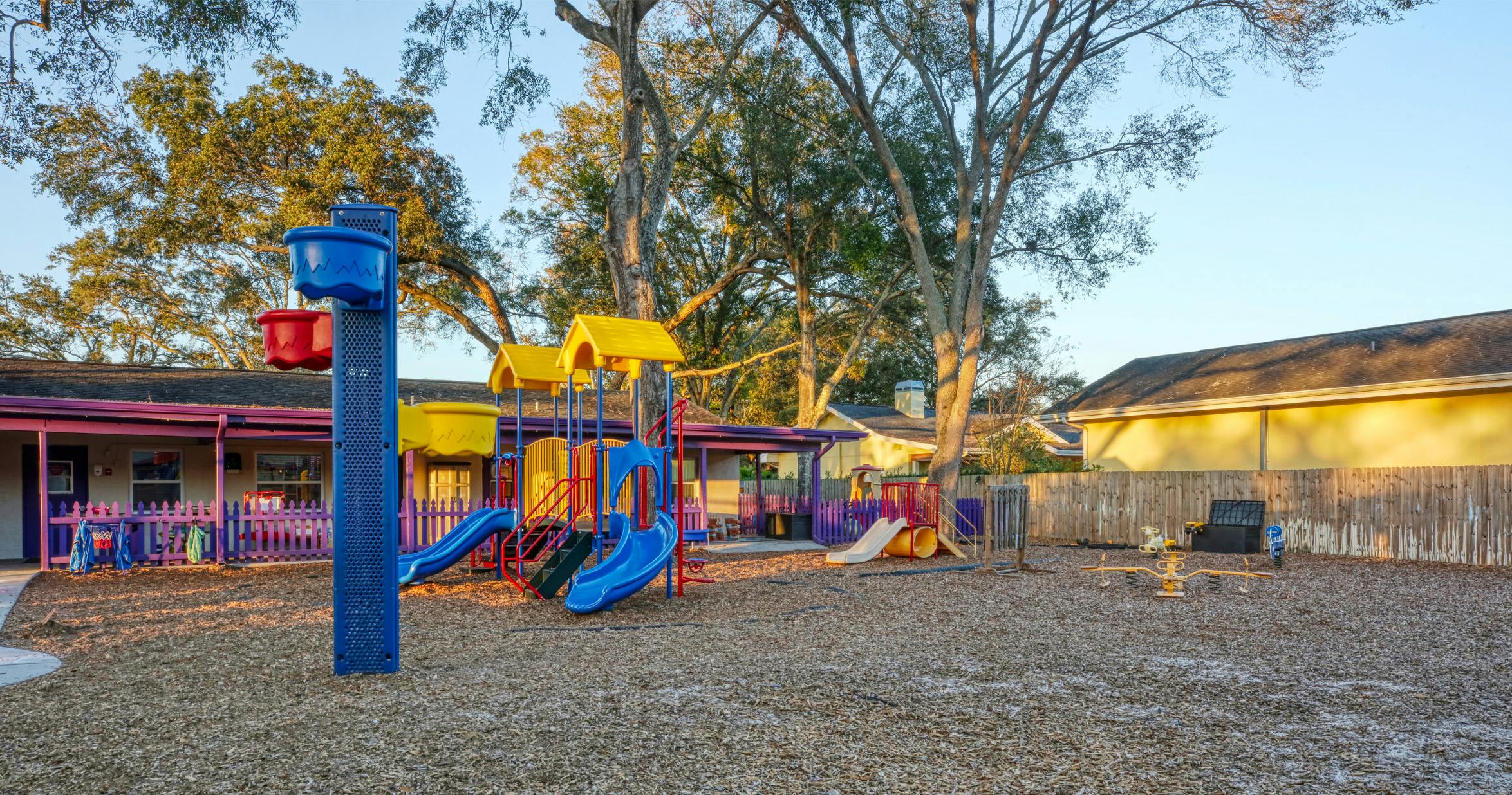 A colorful playground with slides, swings, and a seesaw on wood chips