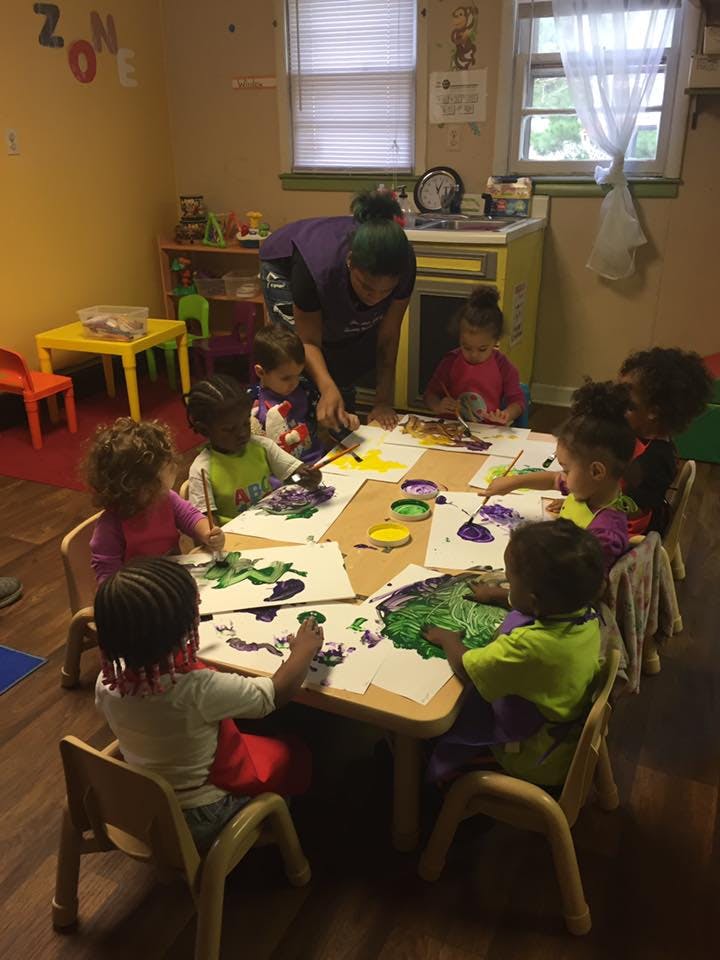 Adult and children painting at a table in a classroom