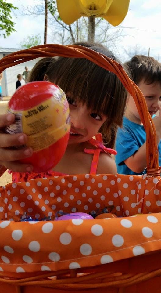 Child holding a large red and yellow egg over an orange polka dot basket