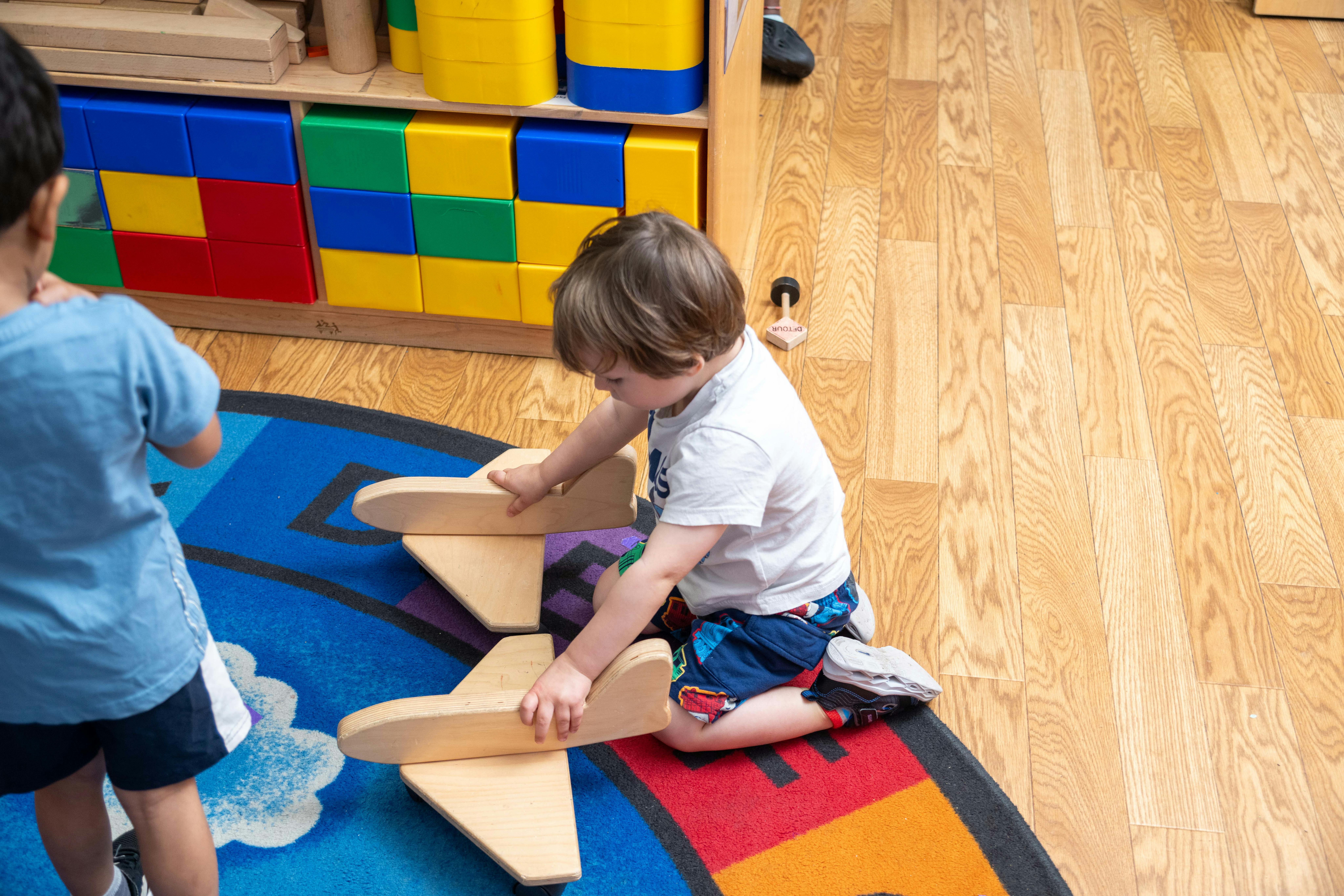 Child playing with wooden airplane toy on a colorful rug