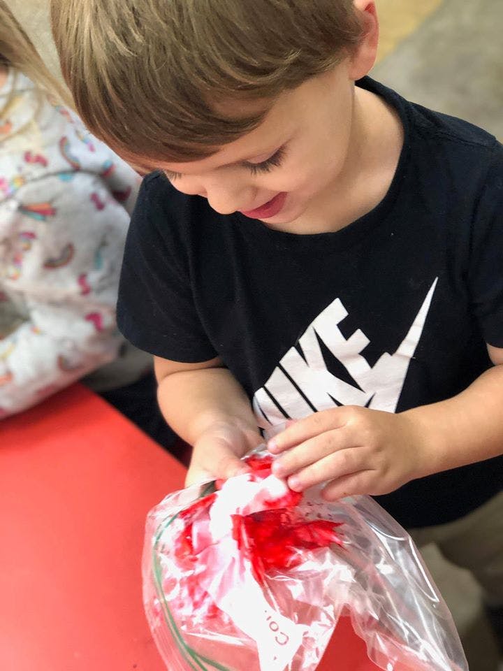 Child mixing red paint in a plastic bag