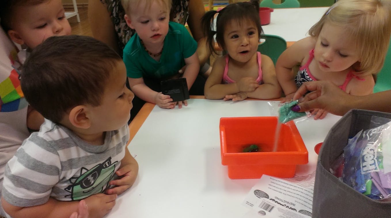Children watching an adult pour something into an orange container
