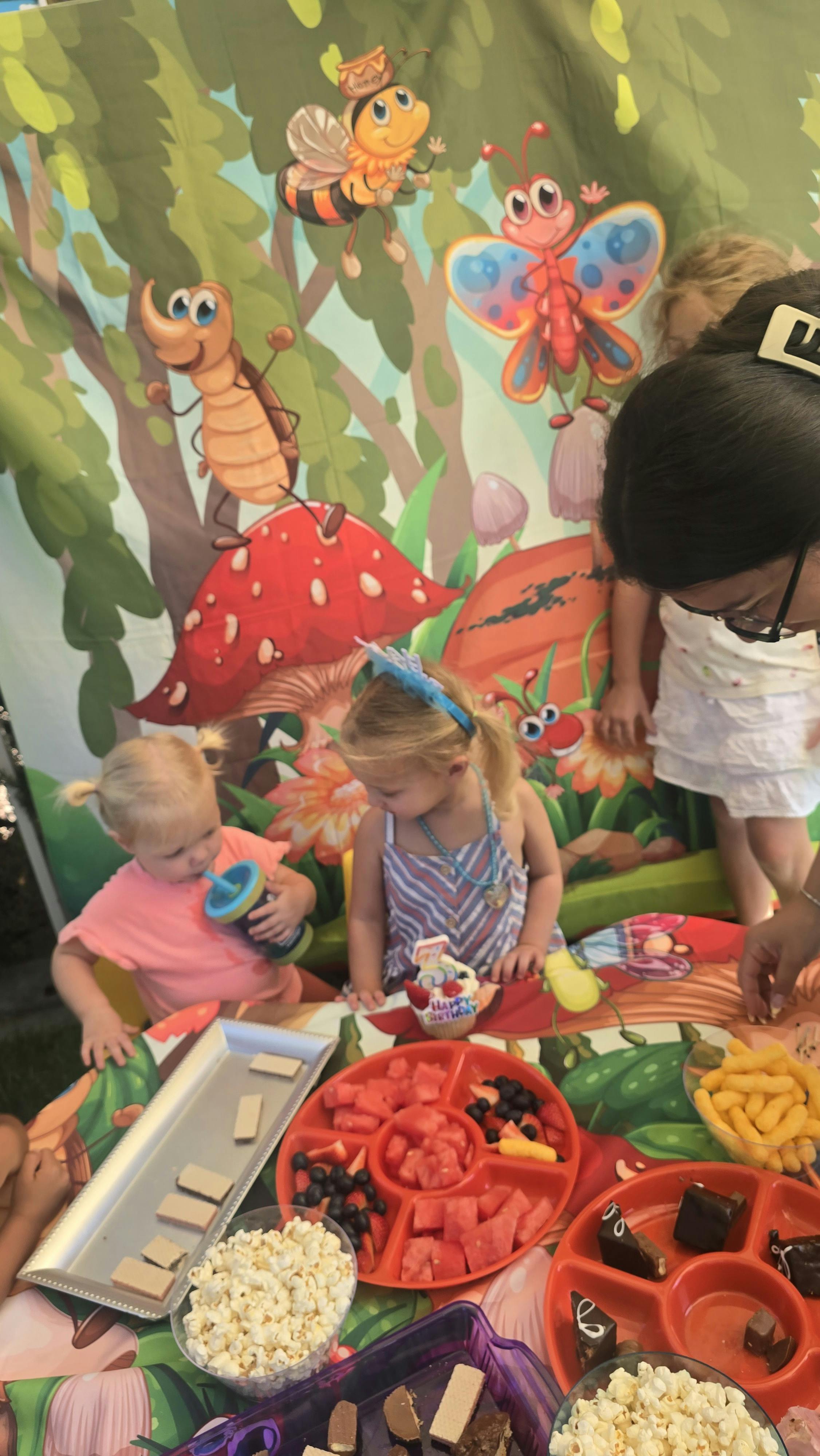 Children gathering around a snack table in front of a garden-themed backdrop