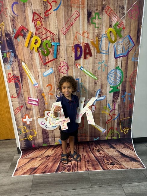 Child holding "4K" letters in front of a "First Day Of" backdrop