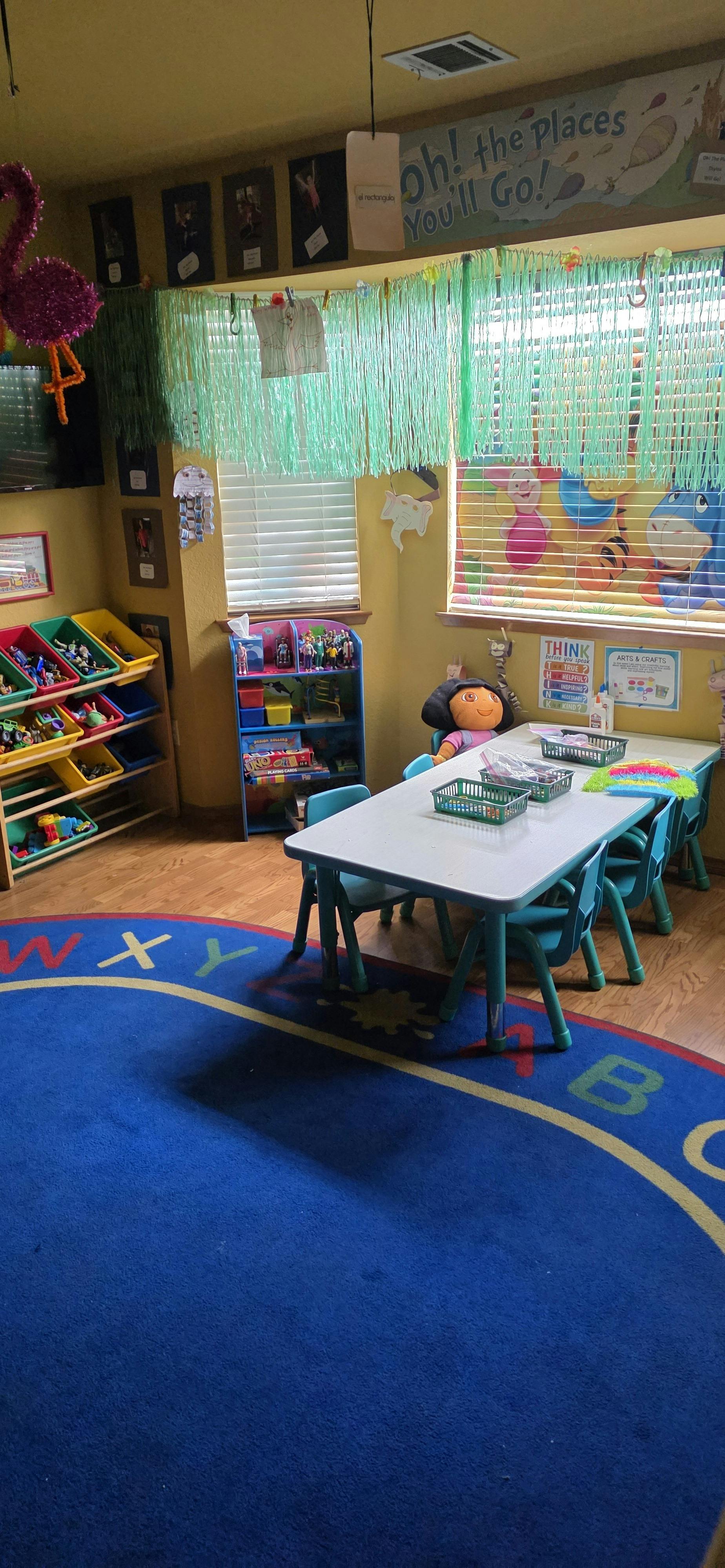 Classroom interior with small table, chairs, toy storage, and alphabet rug