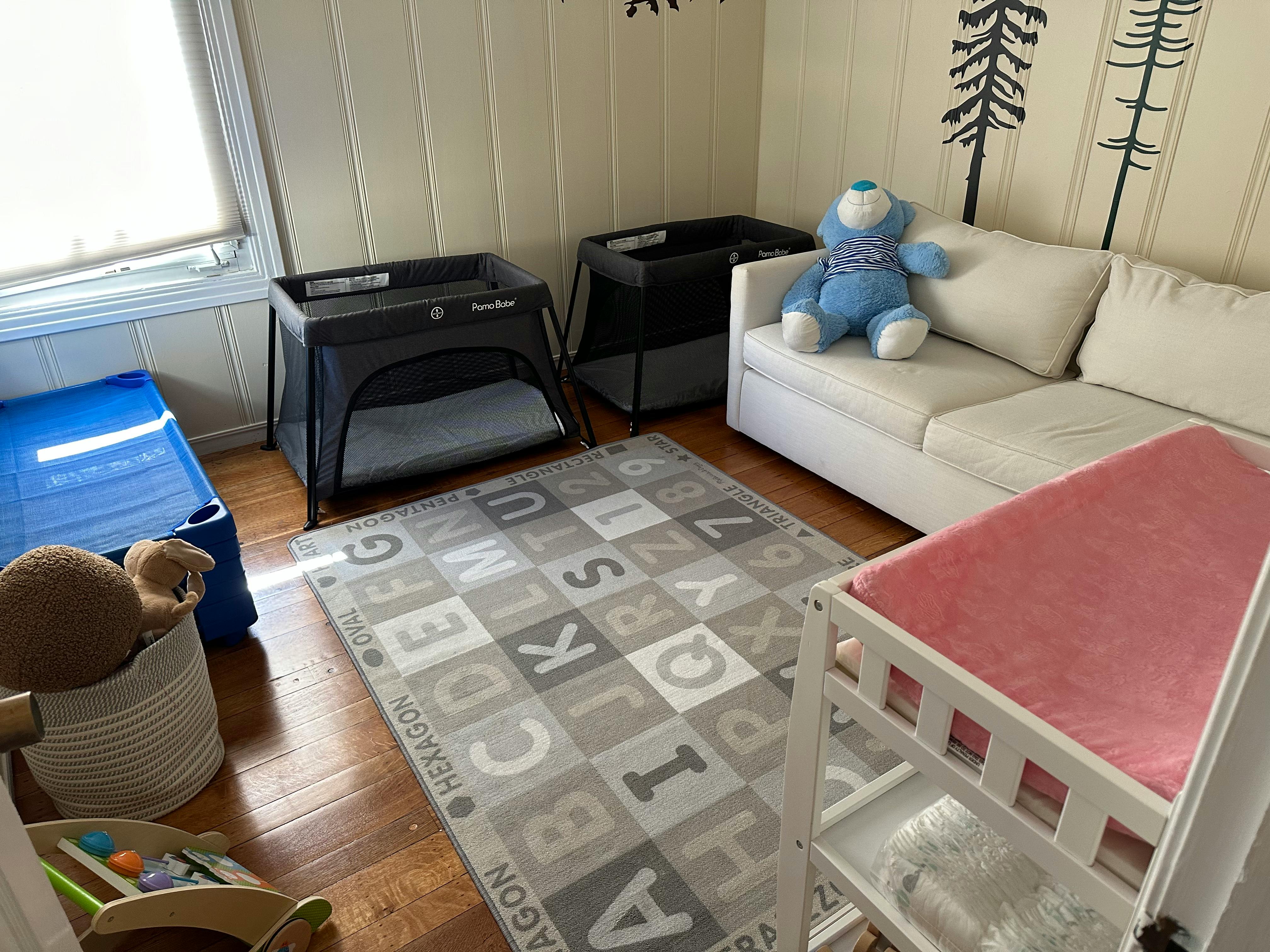 Nursery room with two playards, a white sofa, and a crib