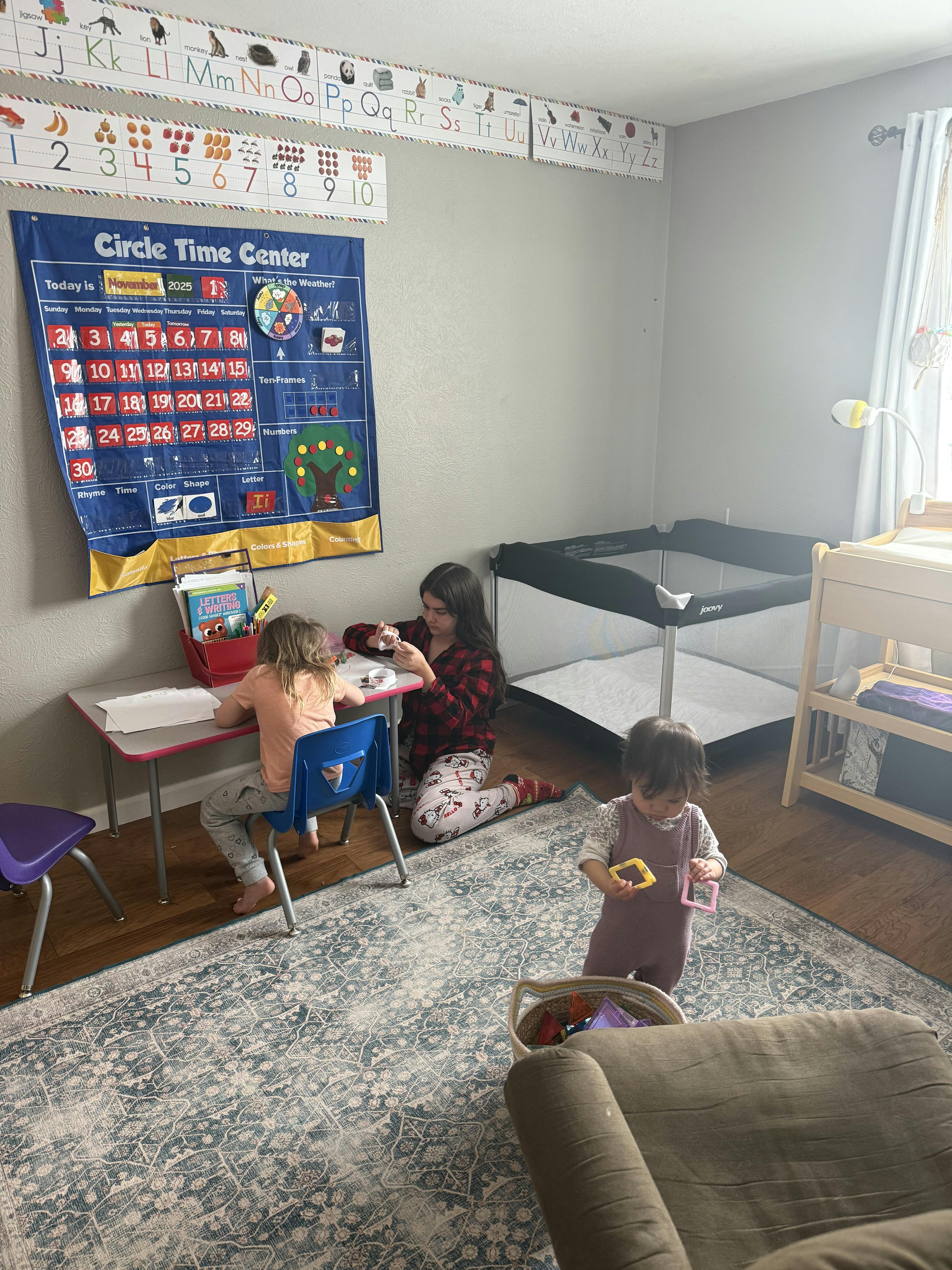 Three children playing in a room with a Circle Time Center chart on the wall