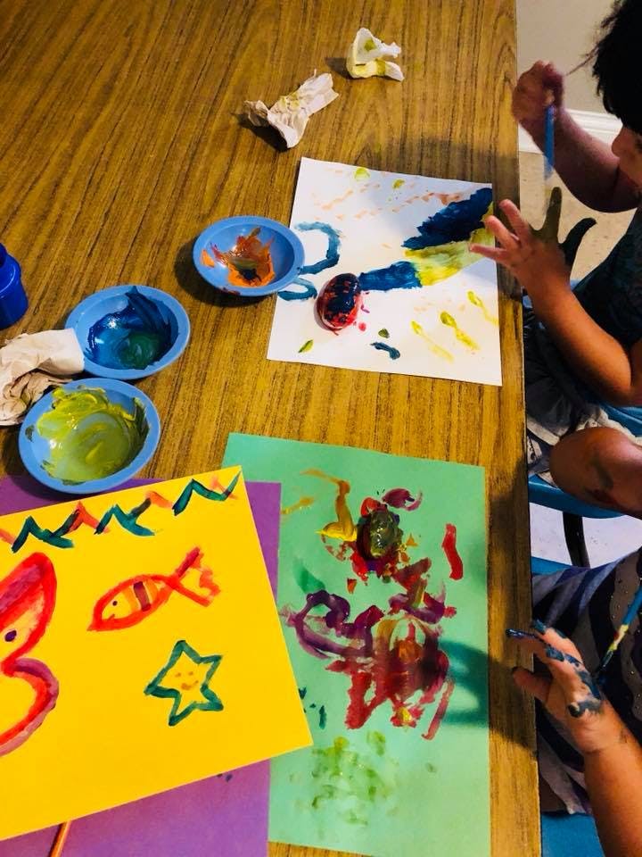 Child painting at a table with multiple colorful art projects and paint bowls