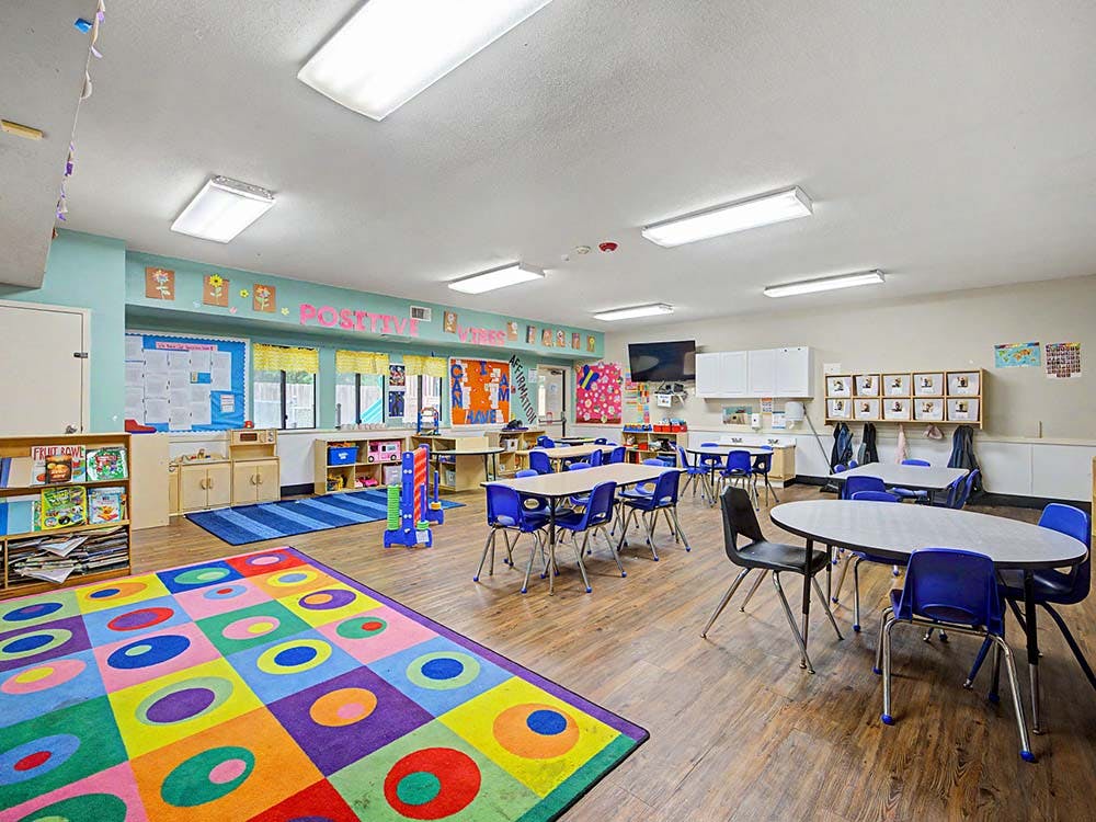 Classroom with small tables and chairs, colorful rugs, and decorations