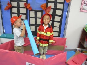 Two children playing in a classroom, one dressed as a firefighter