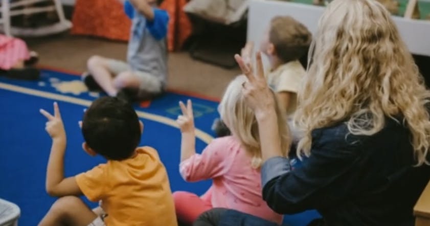 Adult and children sitting on floor, children holding up two fingers