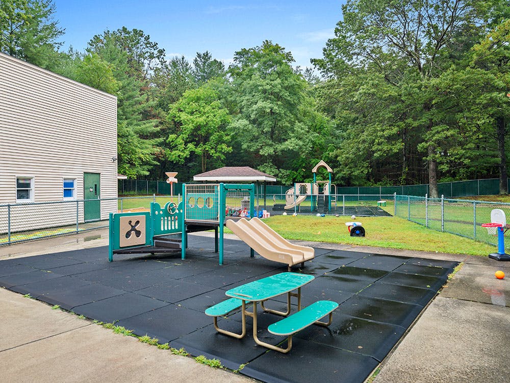 Playground area with slides, swings, and a picnic table, next to a building