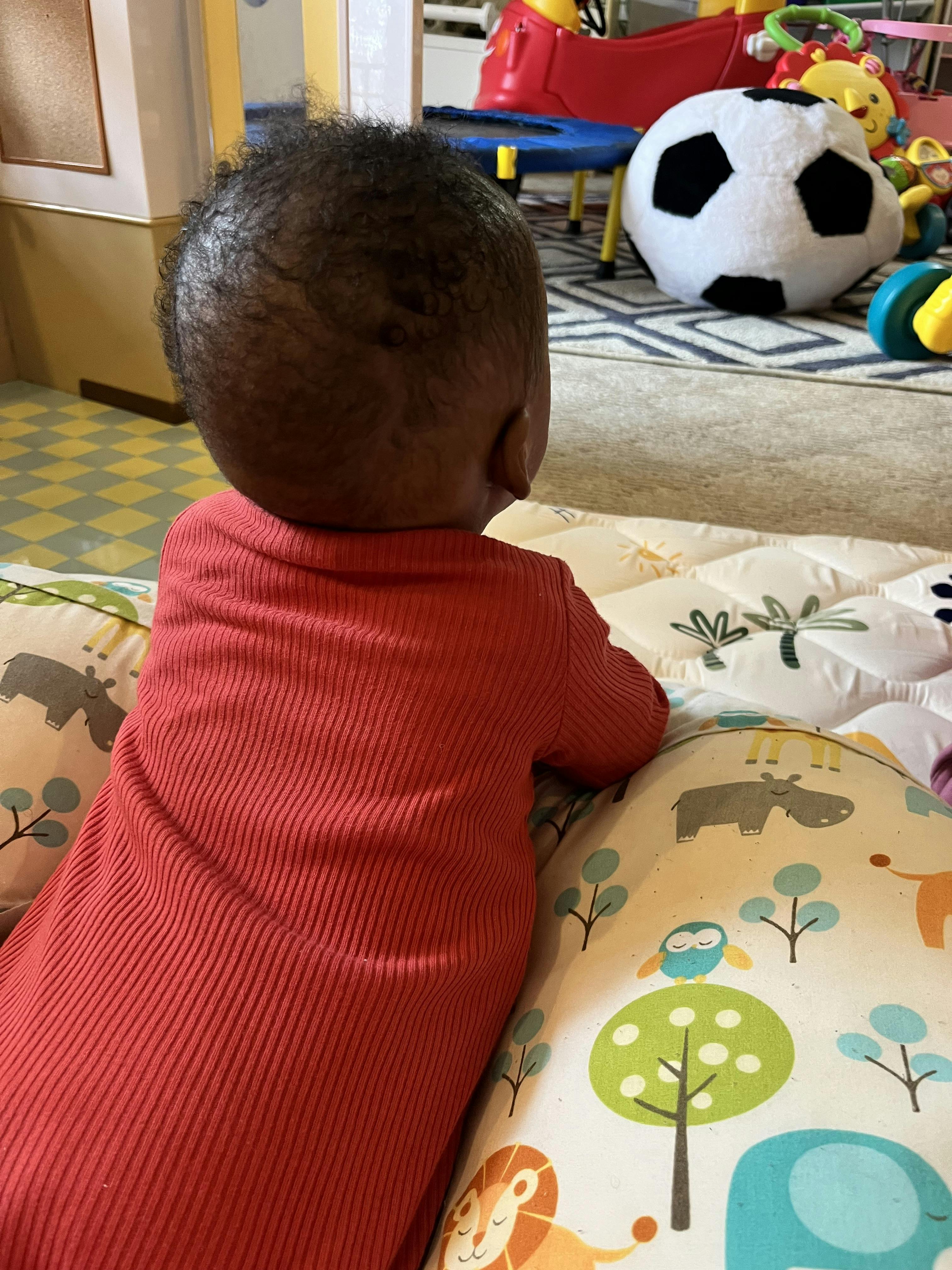 Back of a child's head with curly hair, in a red shirt, on a playmat