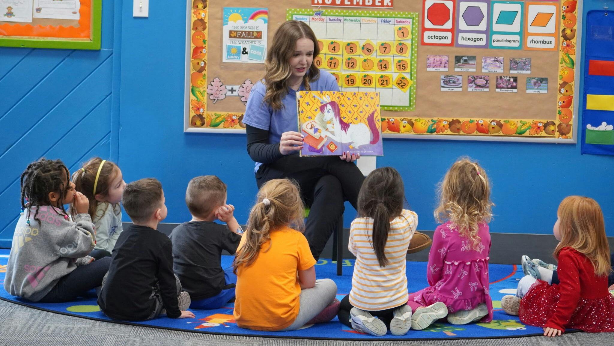 Person reading a book to a group of children in a classroom