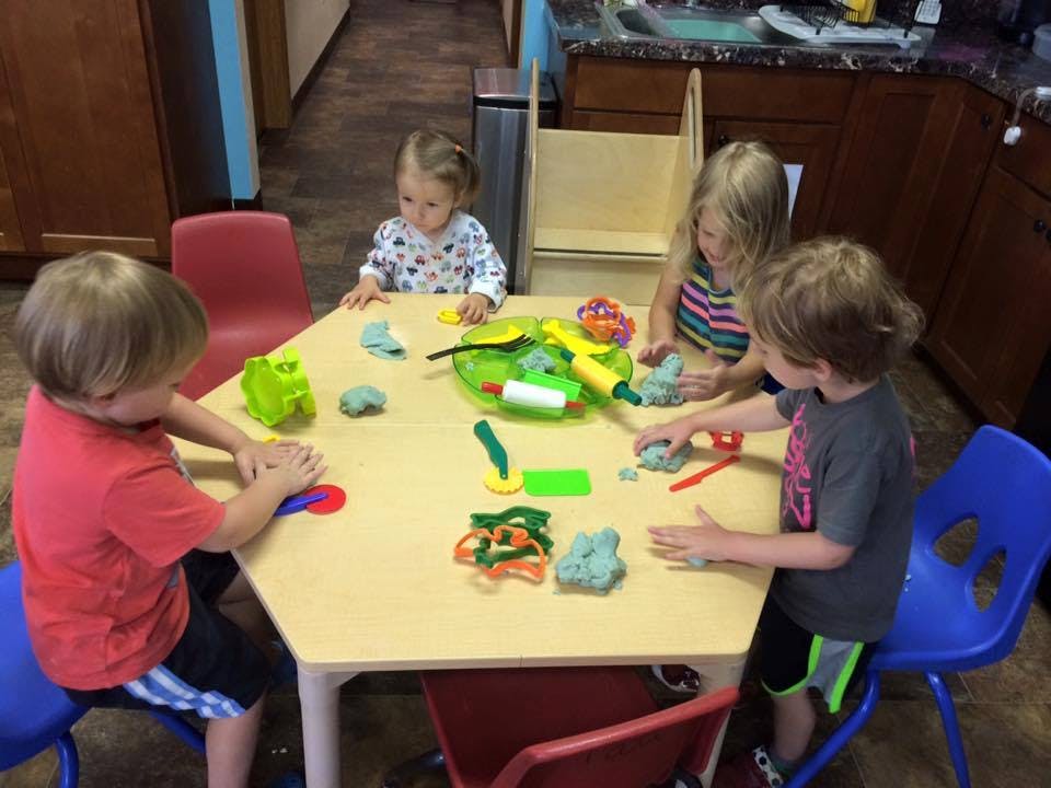 Four children playing with modeling clay at a hexagonal table