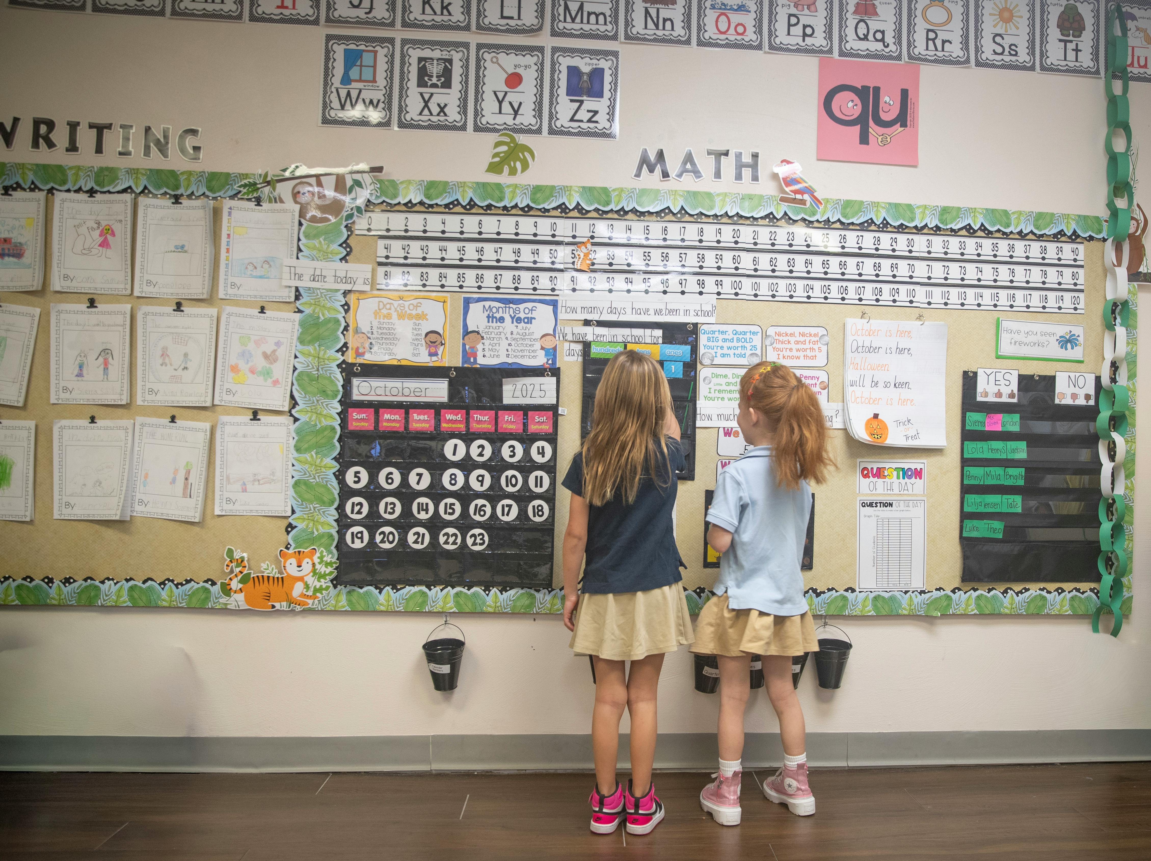 Two children standing in a classroom and interacting with a calendar wall chart