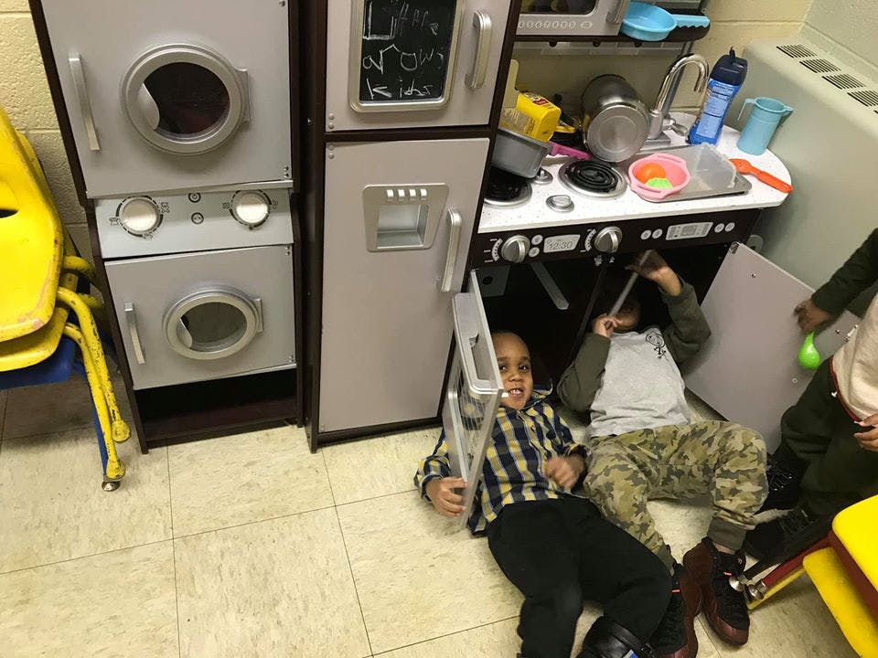 Two children playing on the floor next to a toy kitchen set