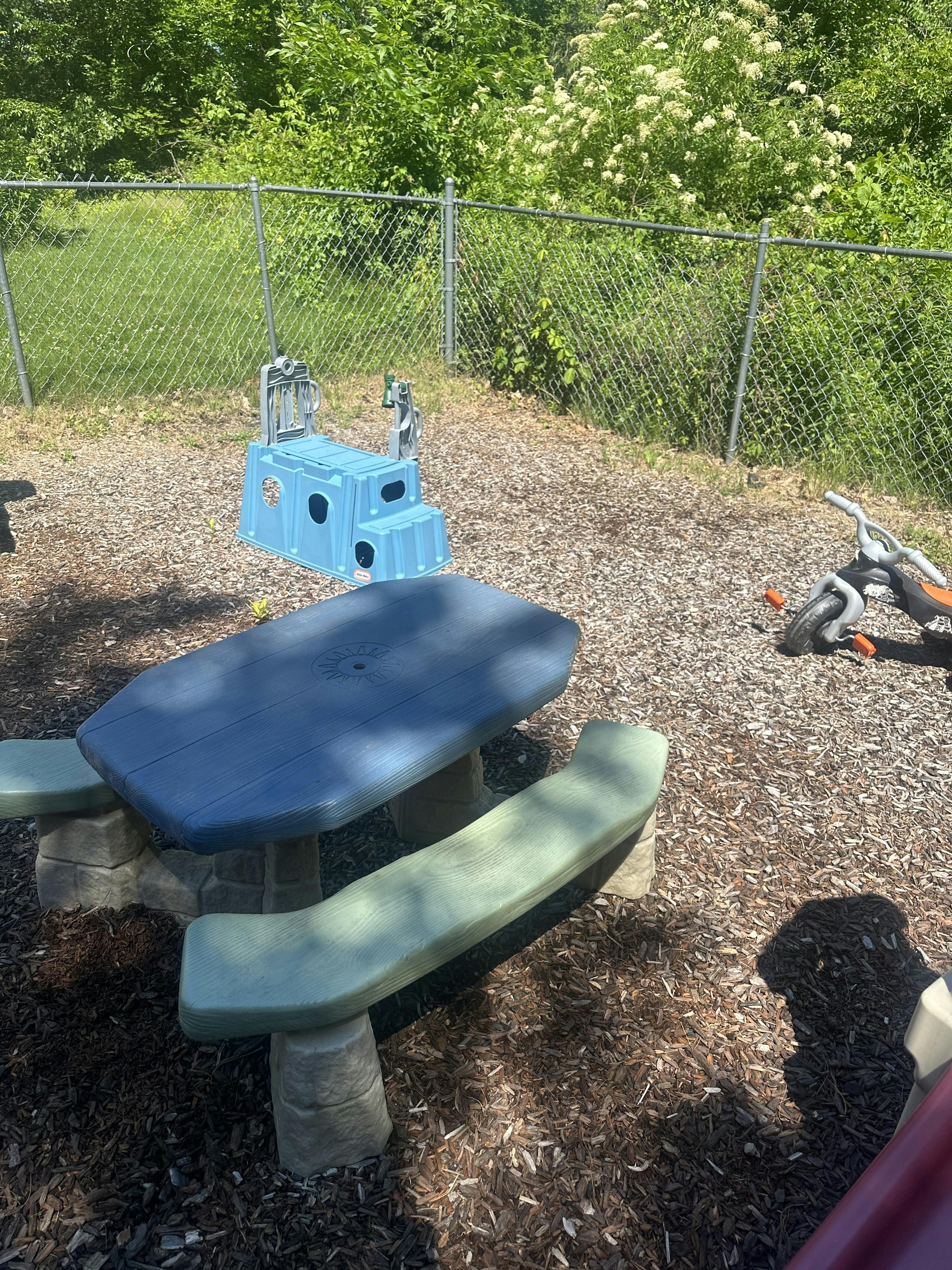 Plastic picnic table and play equipment on wood chips in a fenced yard