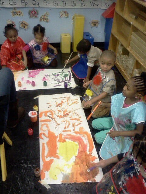Children painting on large sheets of paper on the floor in a classroom