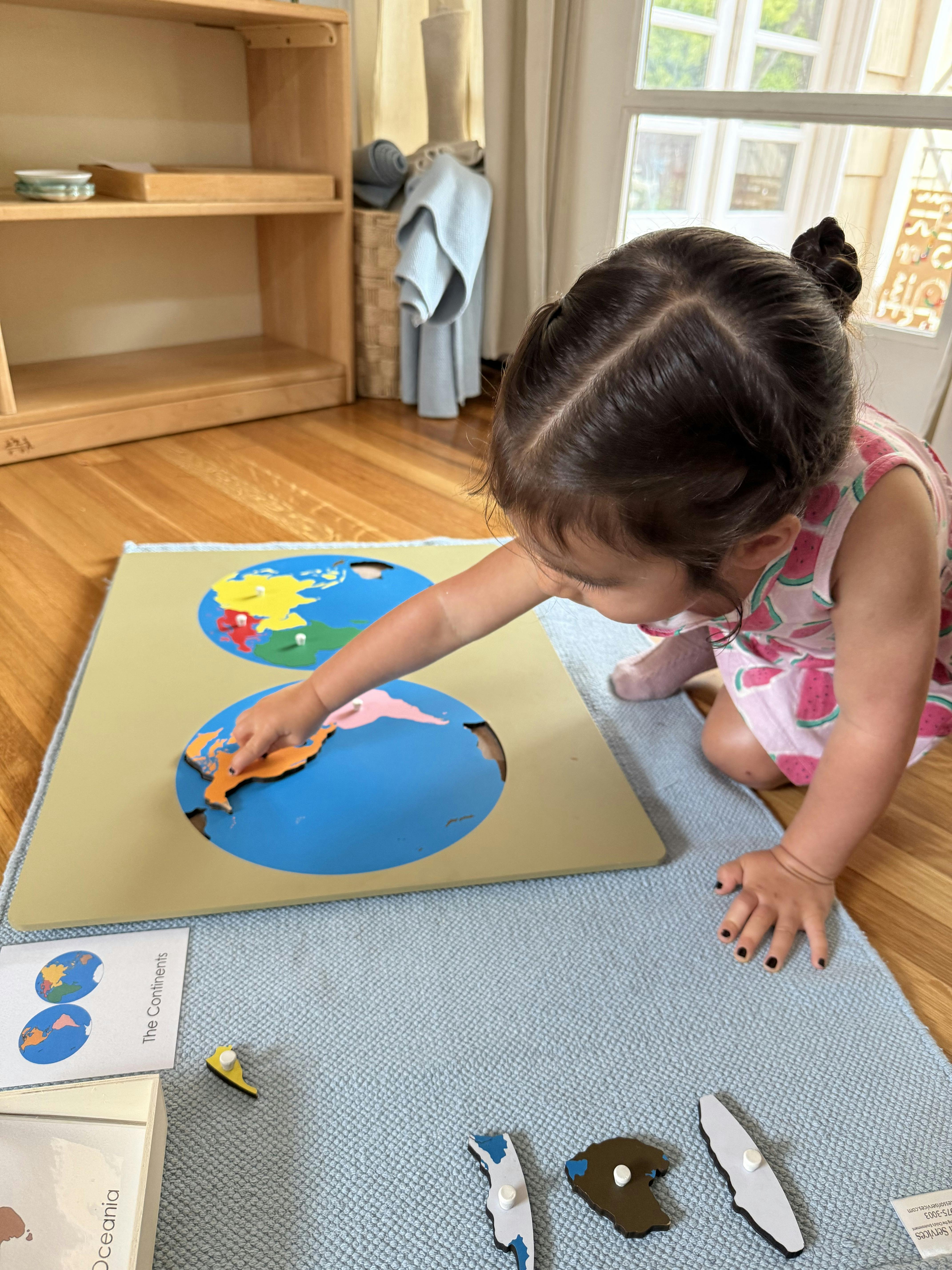 Child placing a continent piece onto a world map puzzle on a floor mat