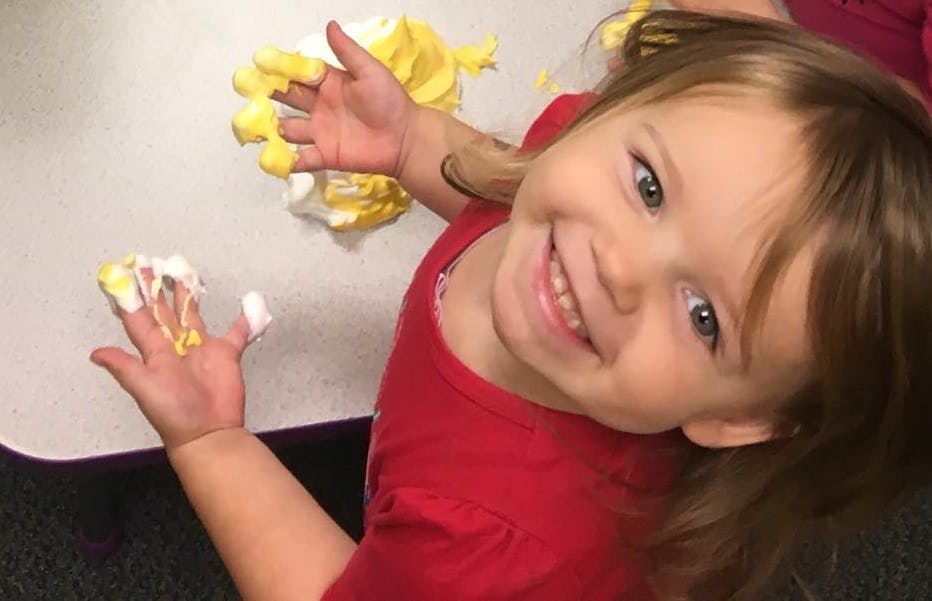 Child with hands covered in yellow and white paint