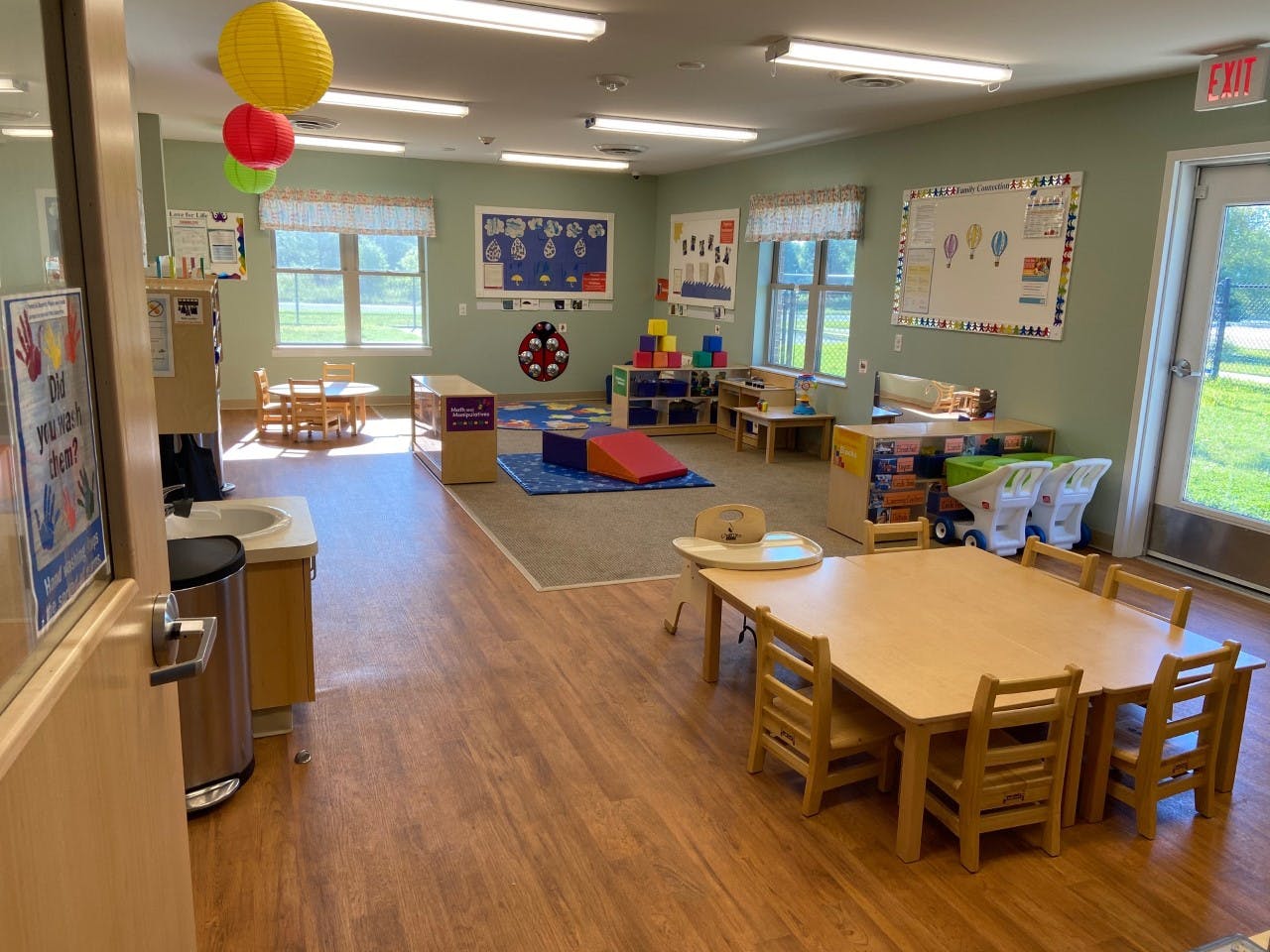 Classroom with small tables and chairs, a sink, and an exit door