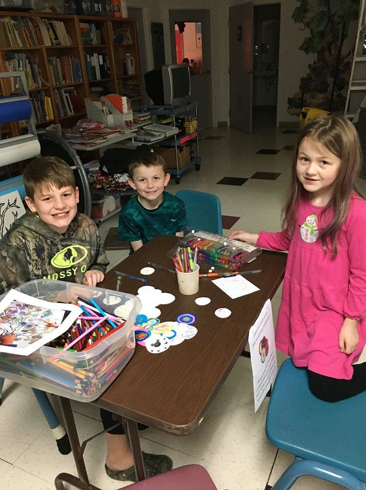 Three children sitting at a table with art supplies
