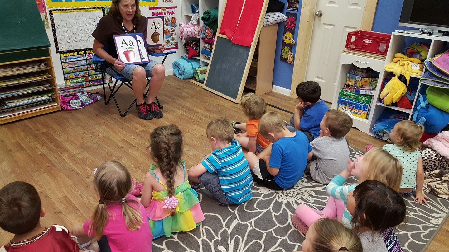 Person reading a book to a group of children sitting on the floor