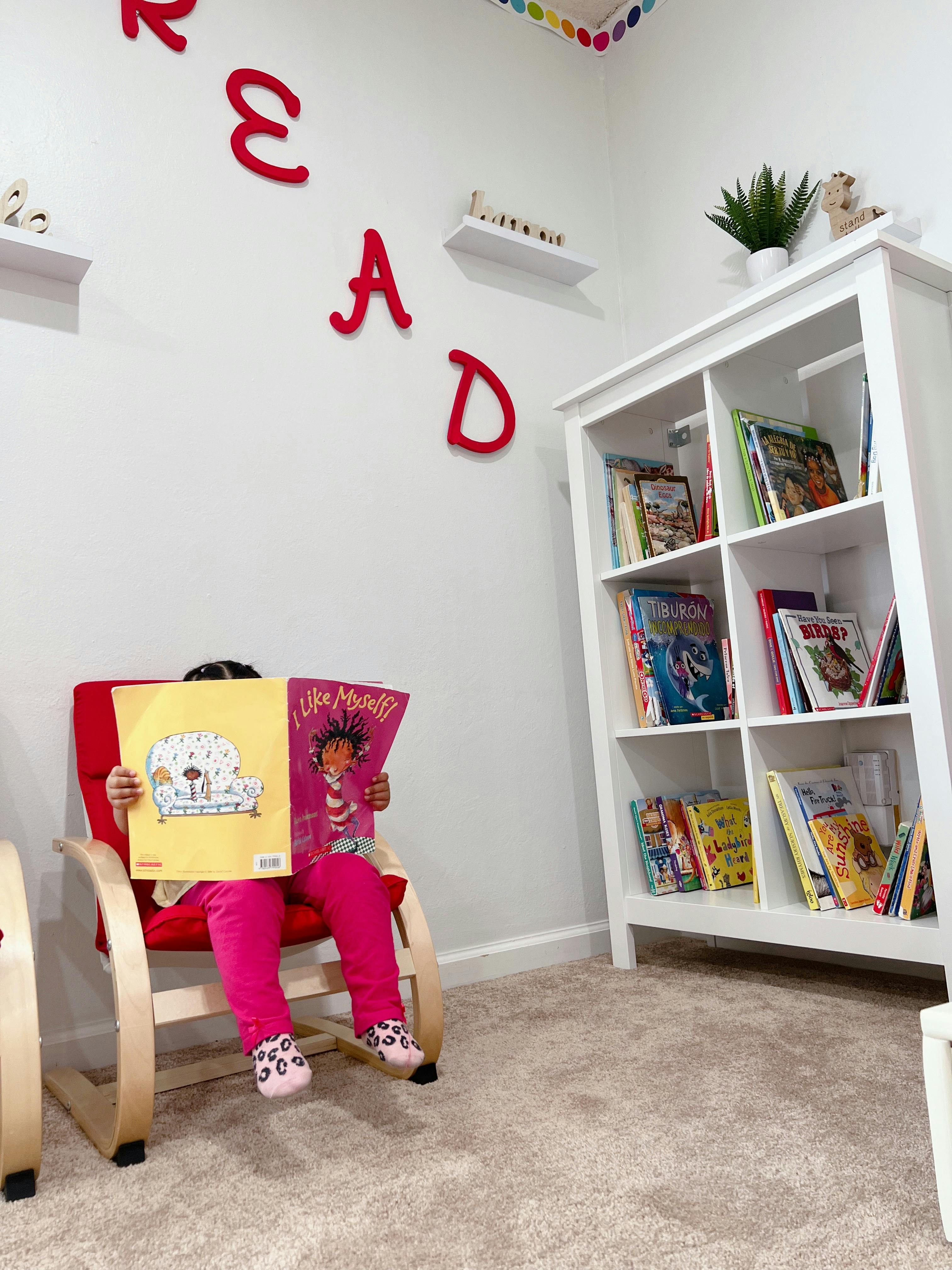 Child sitting in a chair reading a book in a room with a bookshelf