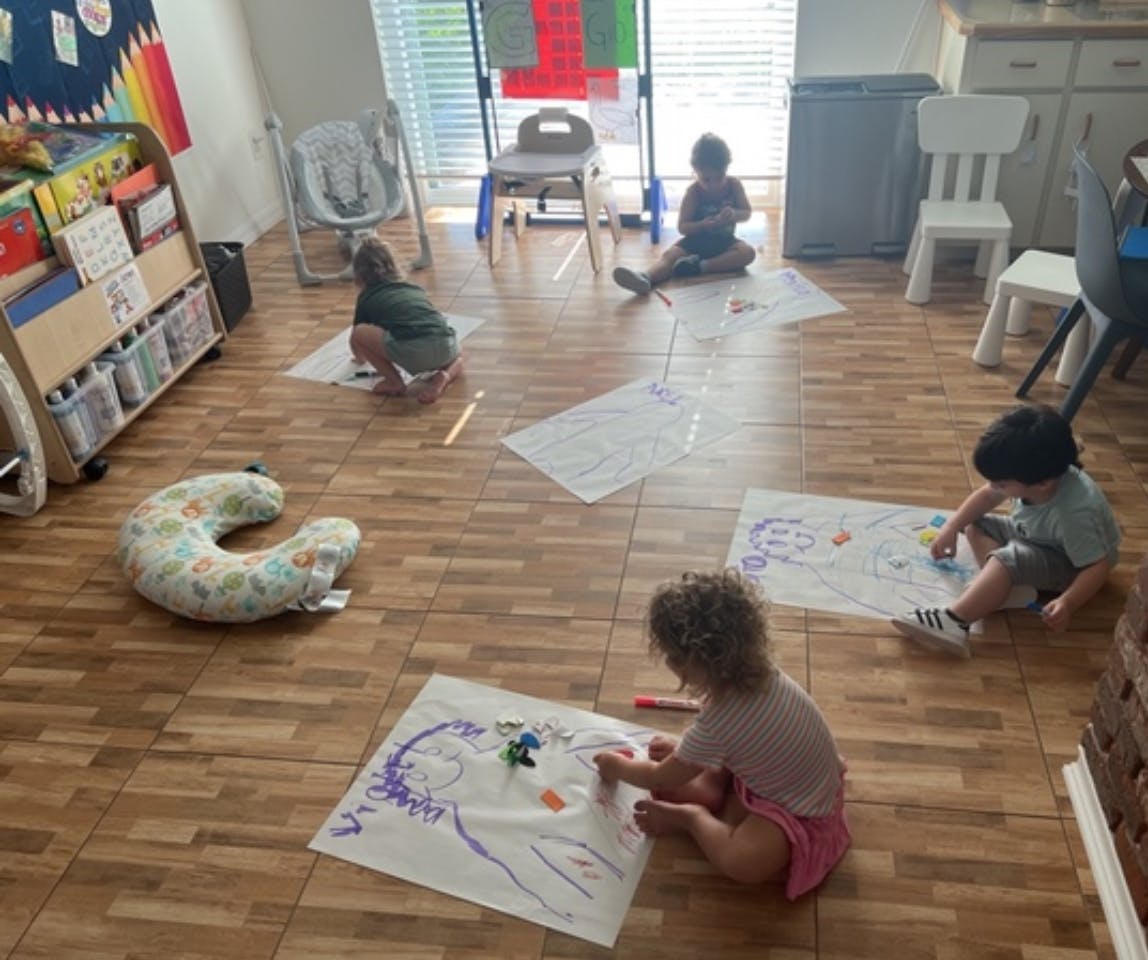 Children sitting on the floor drawing on large sheets of paper