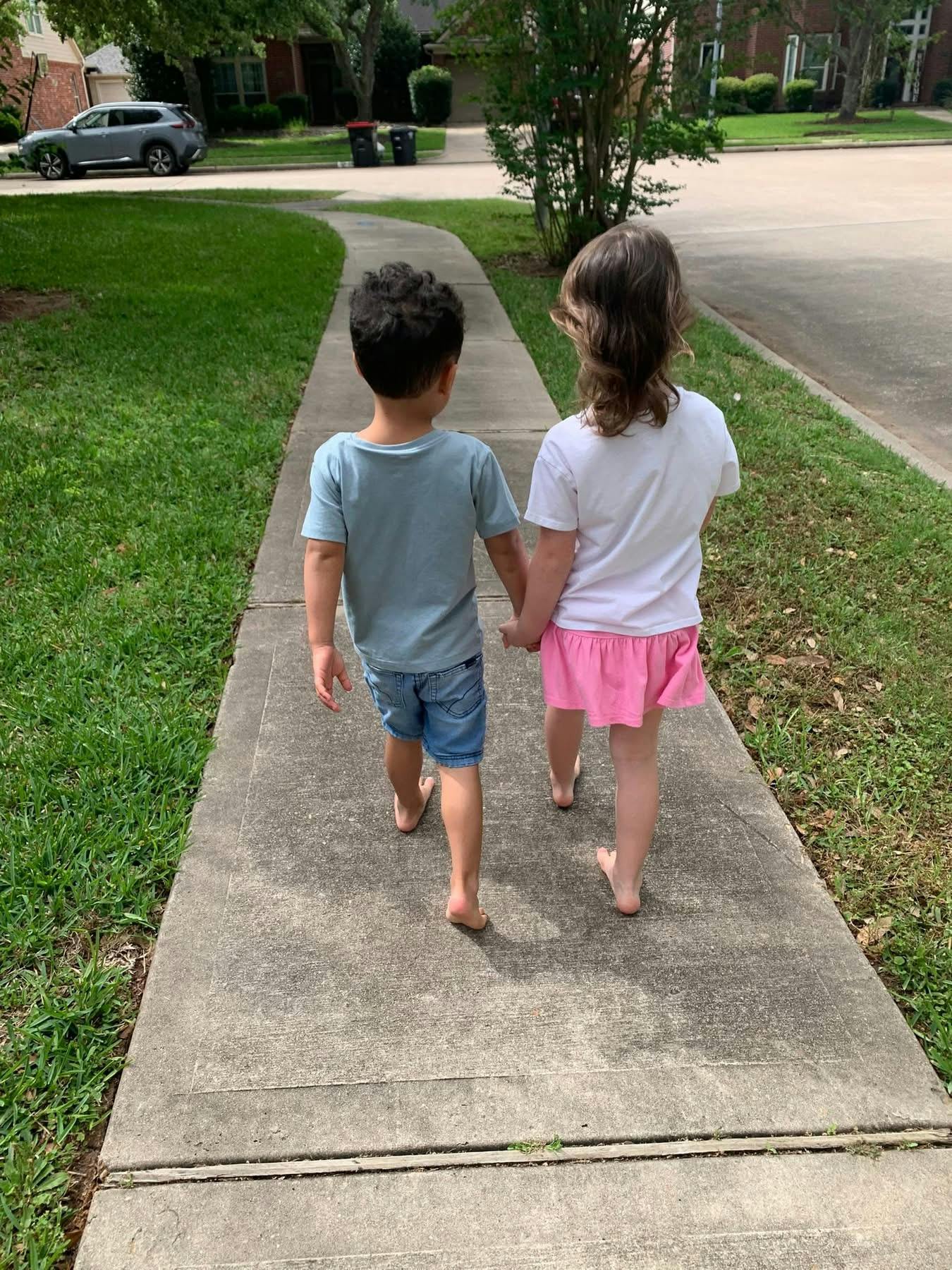 Two children walking barefoot on a sidewalk, holding hands