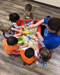 Adult and children playing with sand and toys in a red bin