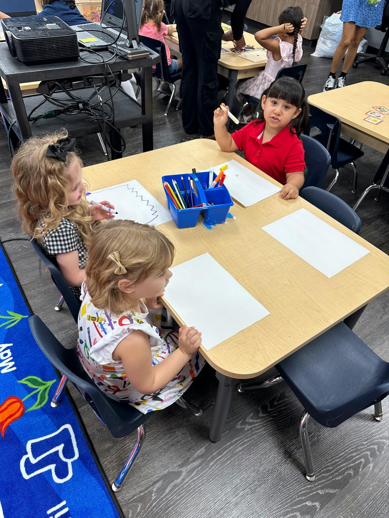 Three children sitting at a table with paper and art supplies