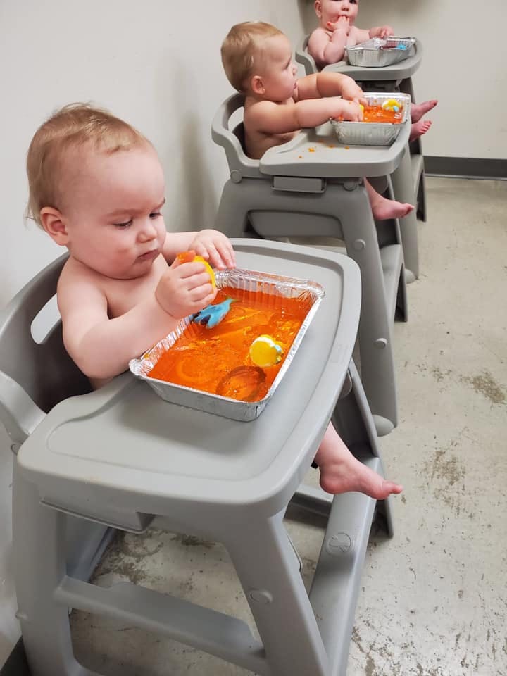 Child in a high chair playing with orange sensory bin