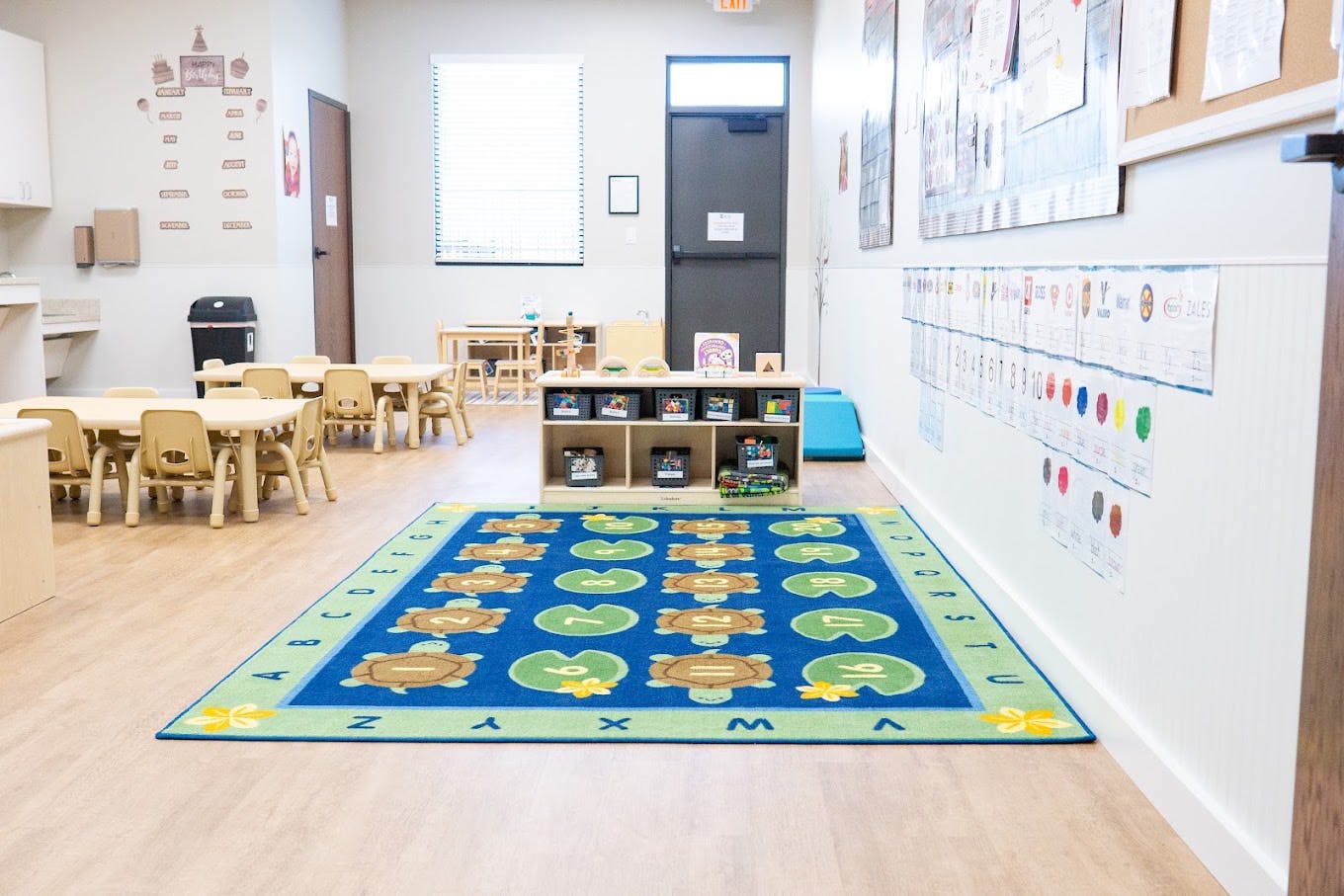 Empty preschool classroom with small tables and a colorful alphabet rug