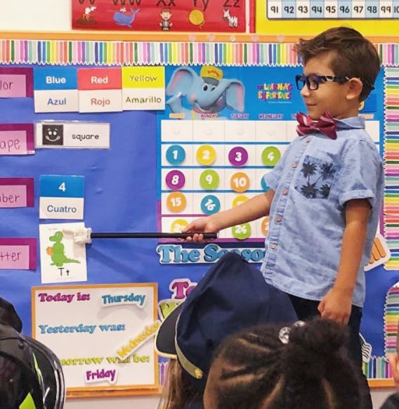 Child in glasses and bow tie pointing to a chart with a pointer