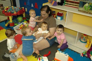 Adult sitting on floor surrounded by multiple babies and young children