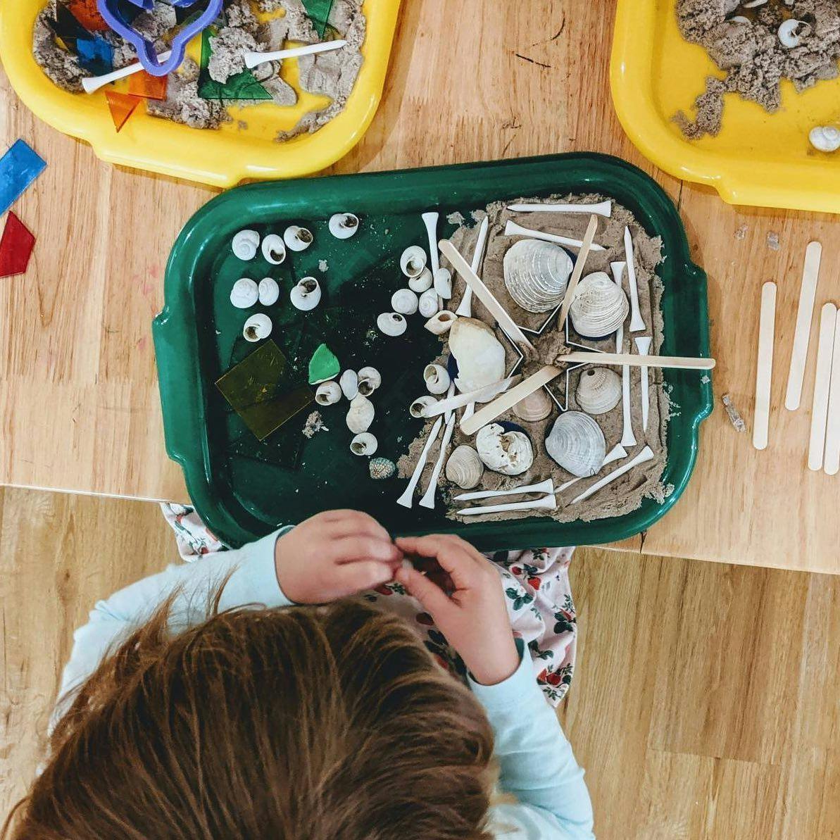 Child playing with sensory bin with shells and golf tees